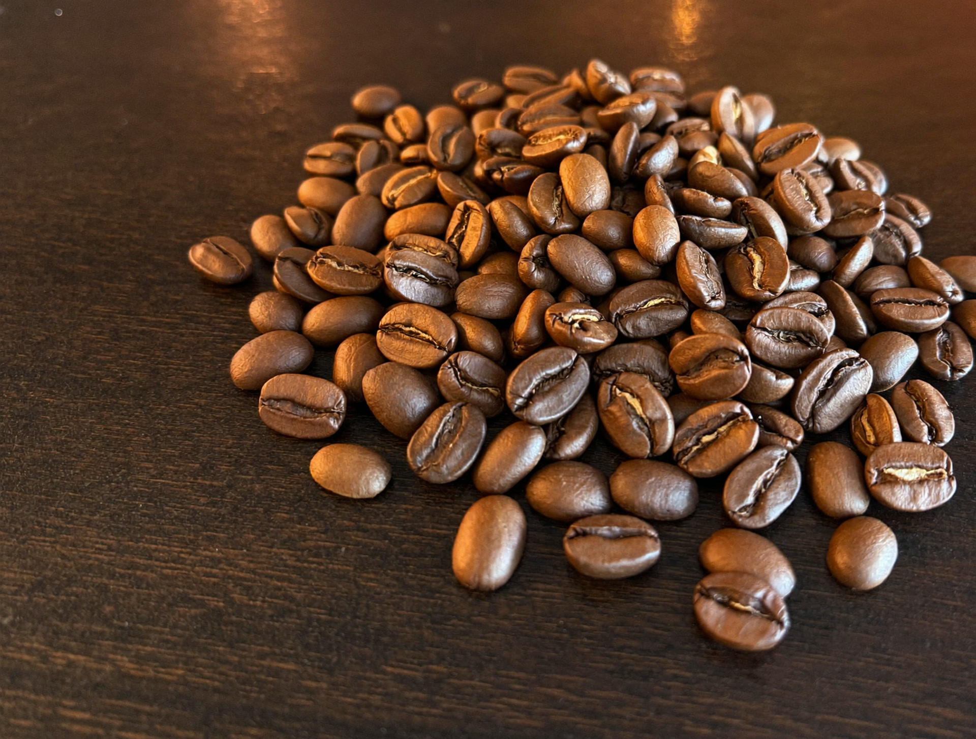 Freshly roasted coffee beans scattered across a dark wood counter.